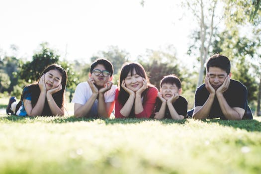 Asian family posing happily on the grass in a sunny park, showcasing love and togetherness.