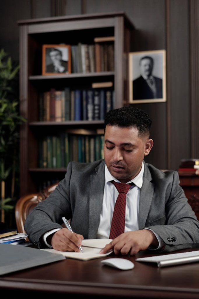 A professional lawyer in a suit sits at a wooden desk in a well-decorated office.