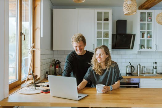 A happy couple enjoying coffee and using a laptop in their stylish, modern kitchen with natural light.